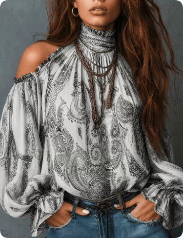 A woman wearing a high-neck, off-the-shoulder blouse with a black and white paisley pattern, paired with blue jeans and layered necklaces, set against a dark gray textured background.