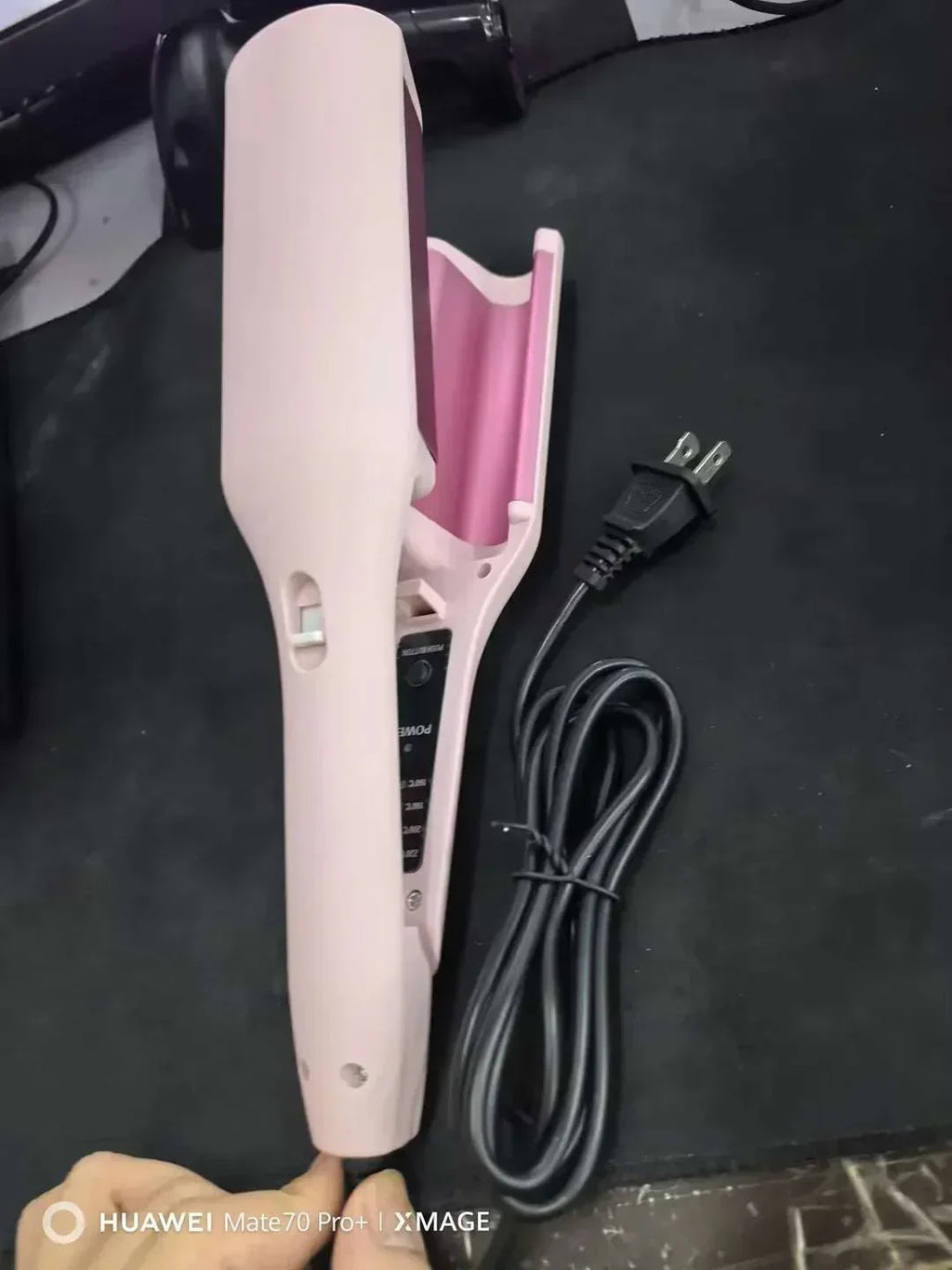 Pink electric hair curler with power cord on black surface