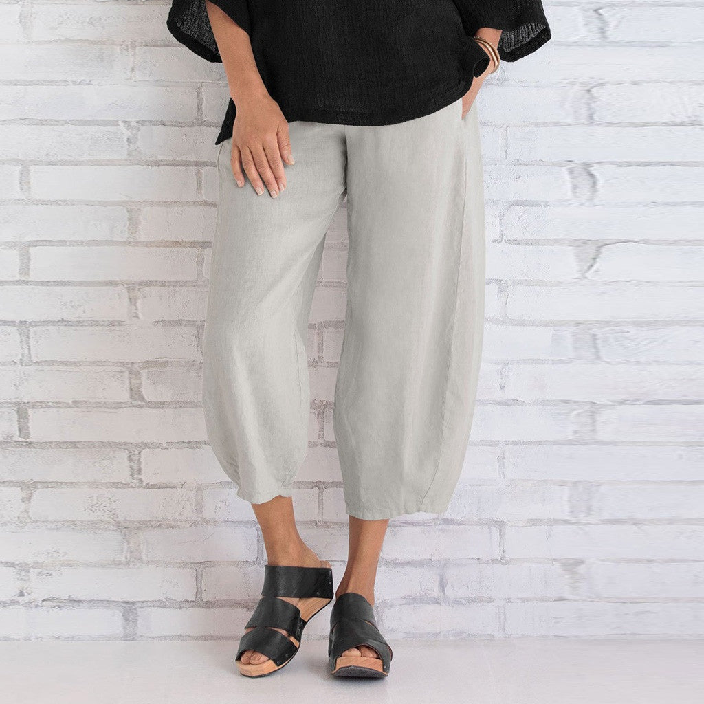 Person wearing light gray pants and black sandals against a white brick wall.