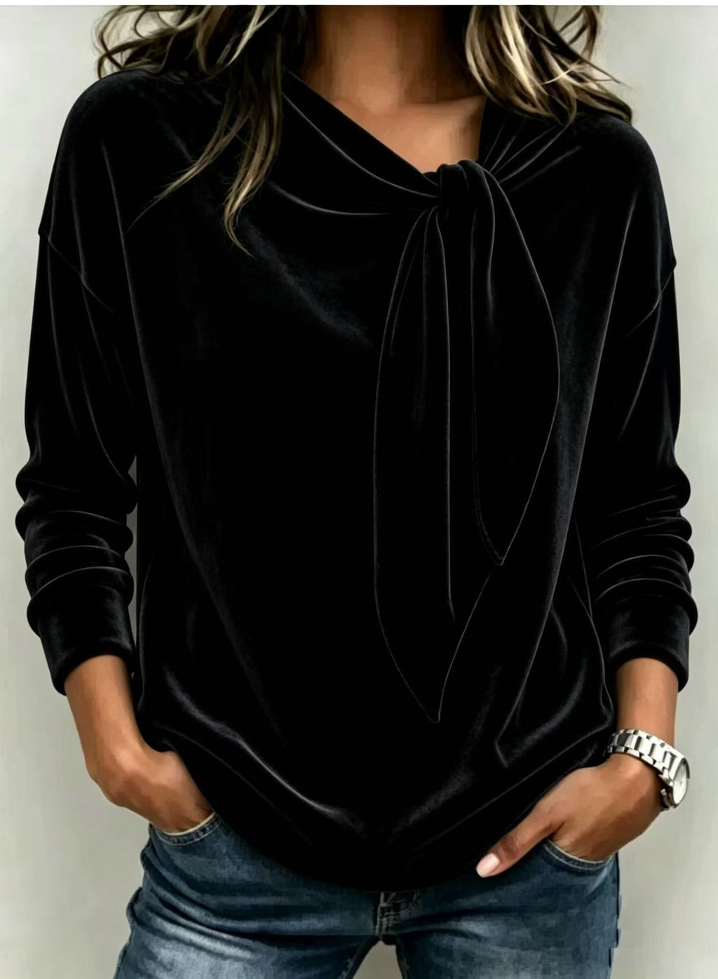 A woman wearing a black velvet long-sleeve top with a cowl neckline and front tie detail, paired with blue jeans.