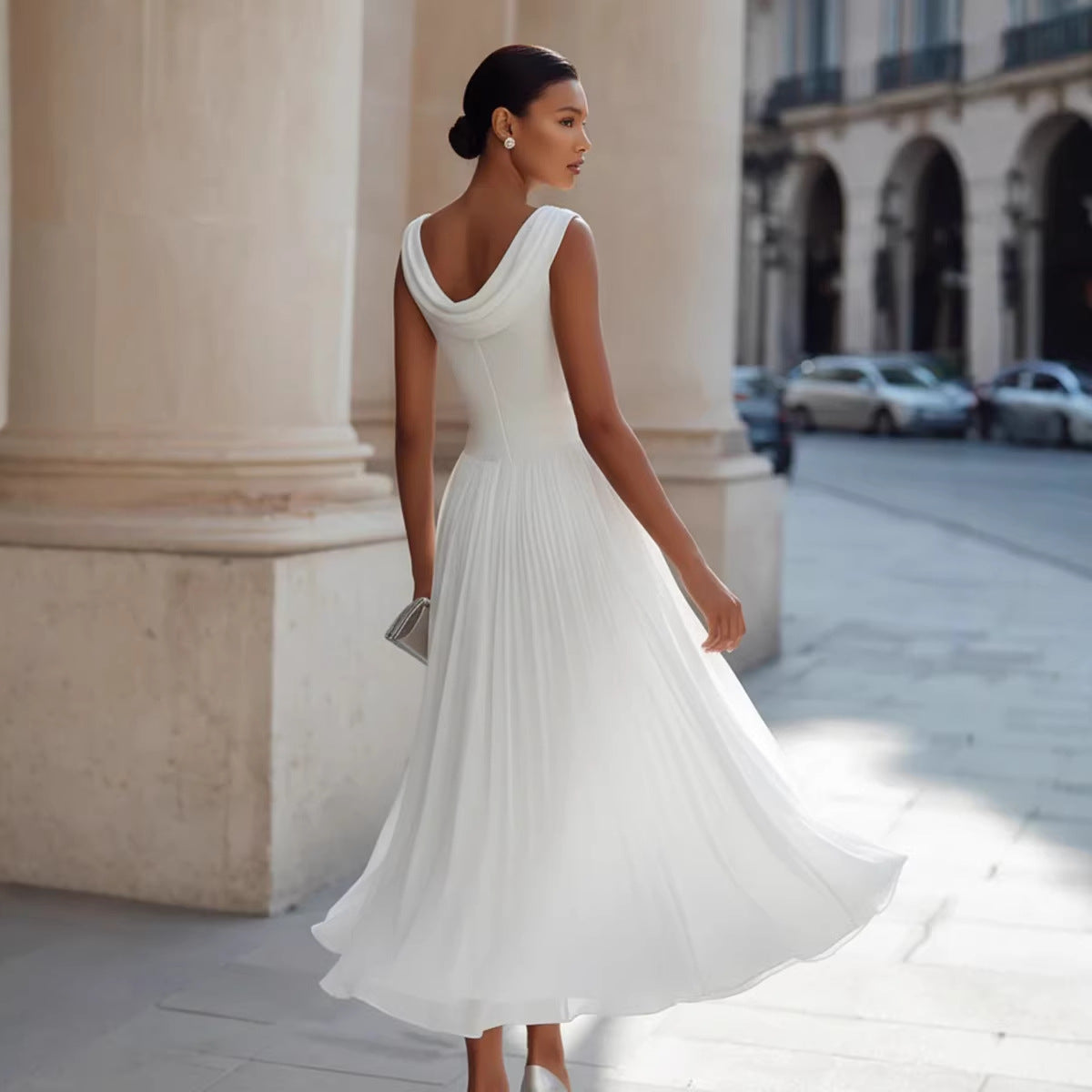 Woman in a white dress walking on a city street with classical architecture.