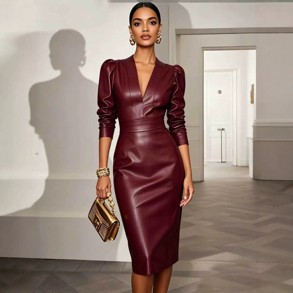A woman models a deep burgundy faux-leather knee-length dress with structured puff sleeves and a plunging V-neckline, holding a gold clutch in a minimalist interior hallway.