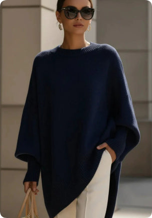 Woman wearing a navy blue poncho with sunglasses and holding a handbag.