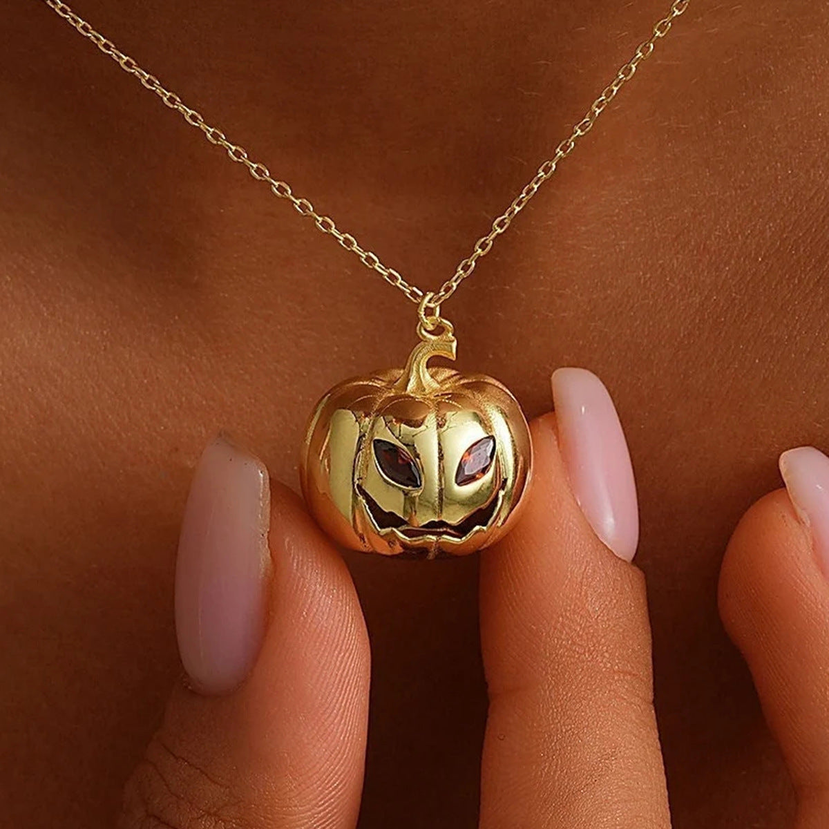 Gold pumpkin-shaped pendant necklace on a person's hand with a brown background