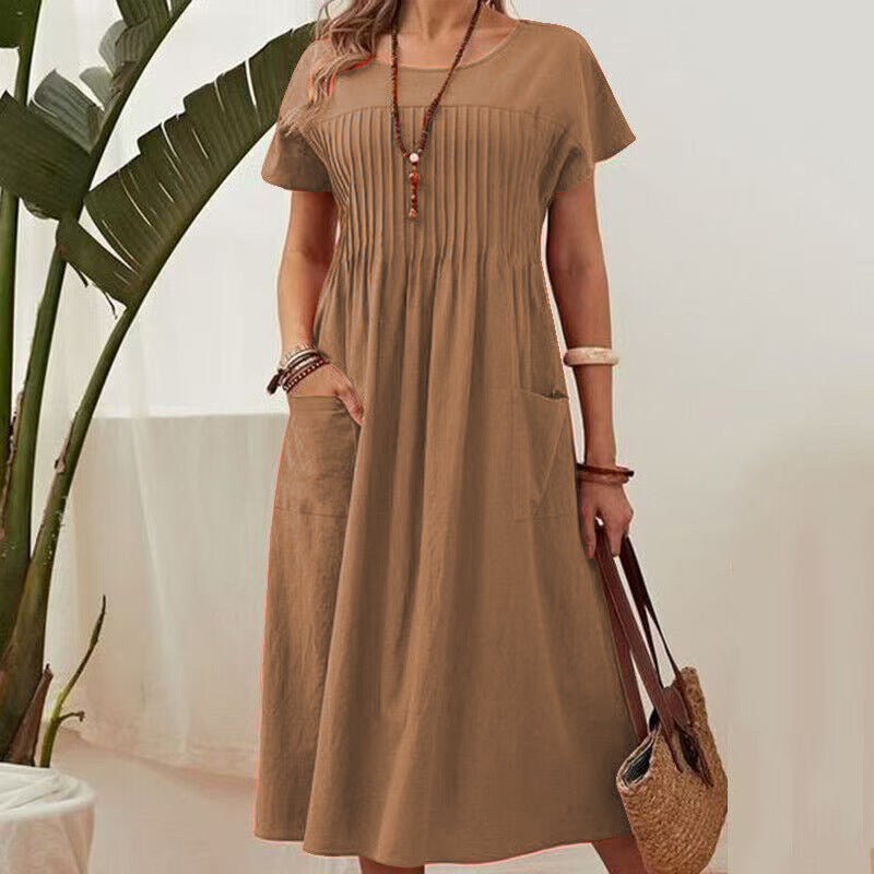Woman wearing a brown dress holding a straw bag with a plant in the background