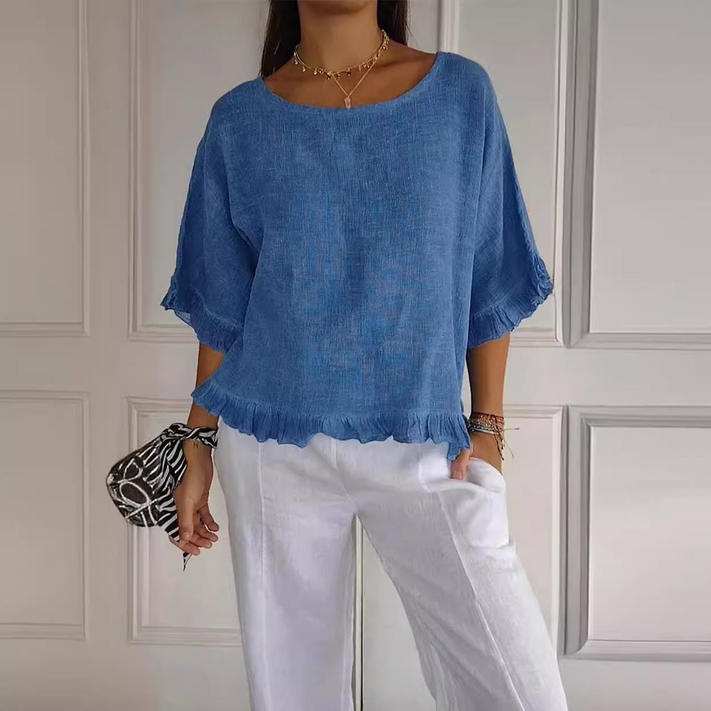 Person wearing a blue top and white pants against a neutral wall.