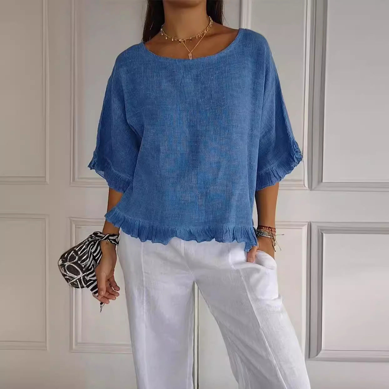 Person wearing a blue top and white pants against a neutral wall.