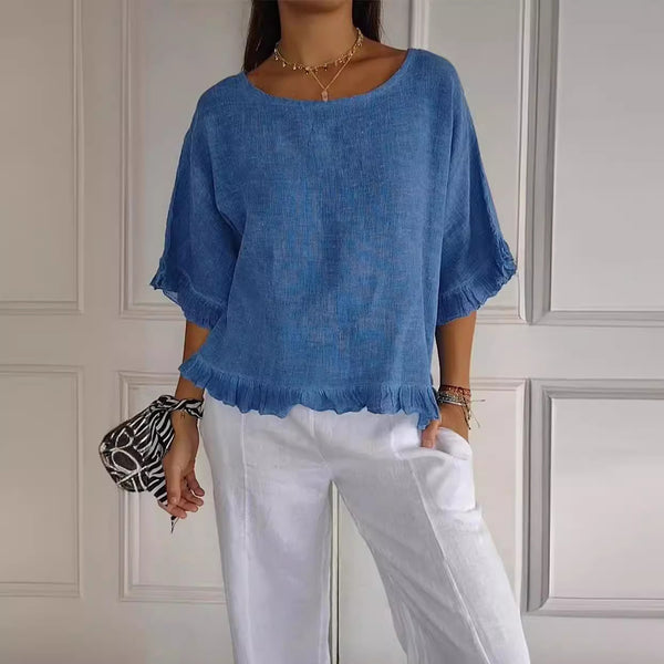 Person wearing a blue top and white pants against a neutral wall.