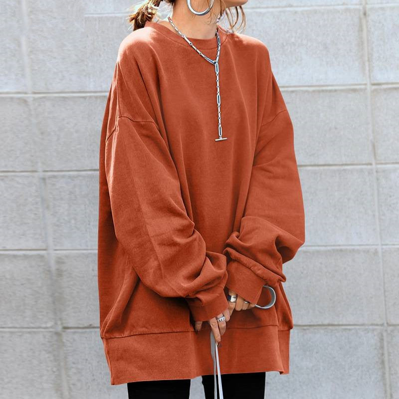 Person wearing a rust-colored oversized sweatshirt against a light gray tiled wall.