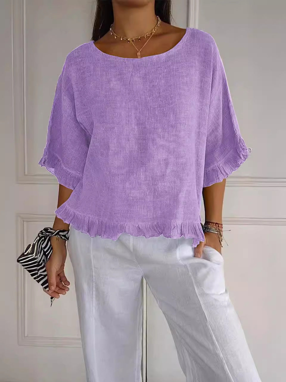 Person wearing a purple top and white pants against a neutral background