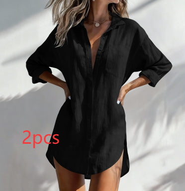 A woman wearing a loose black button-front shirt dress with three-quarter sleeves and side pockets, standing against a white wall with soft shadows. Red text overlay reads '2pcs'.