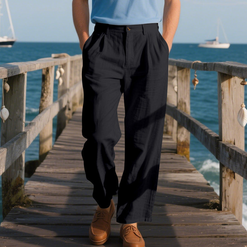 Person wearing black pants and brown shoes on a wooden pier with ocean and sailboats in the background