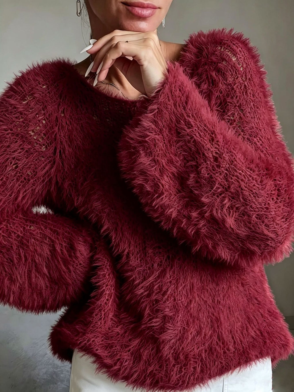 A close-up of a woman wearing a chunky, long-sleeve fuzzy knit sweater in a deep burgundy red, paired with white pants.