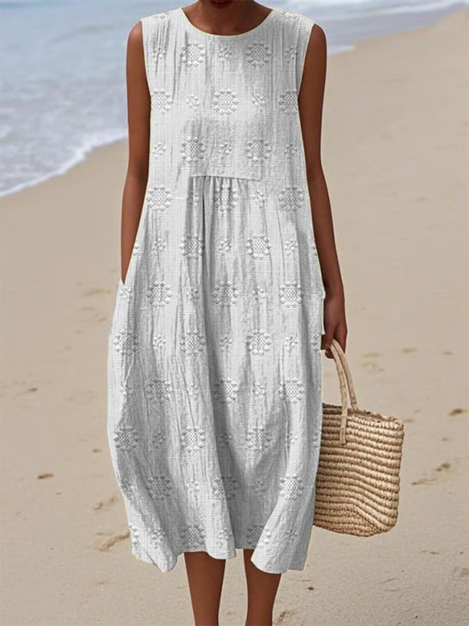 Woman wearing a white sleeveless dress with black patterns on a beach.