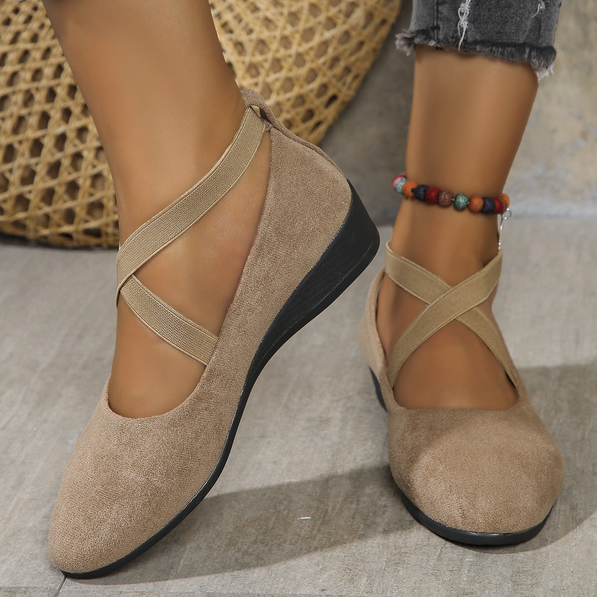 Beige flat shoes with criss-cross straps worn by a person on a neutral background