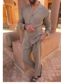 Man in a beige outfit standing in front of a building with columns.