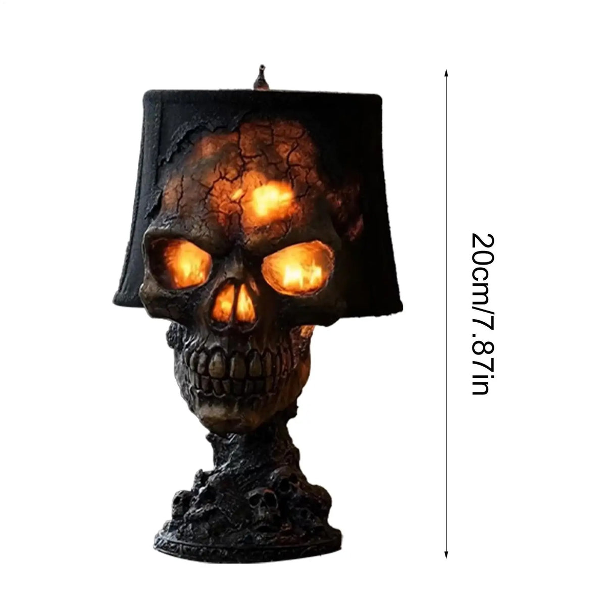 A skull-shaped table lamp with a black lampshade and a dark textured base, glowing with warm orange light from within the eye sockets and top crack detail. A vertical measurement marker on the right reads 20cm / 7.