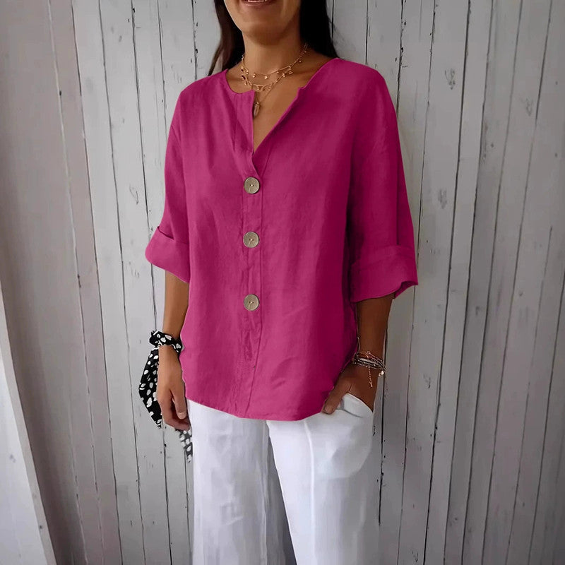 Person wearing a bright pink blouse with buttons and white pants against a wooden panel background