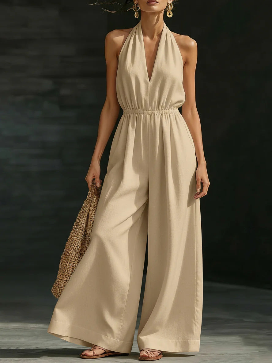 Woman wearing a beige jumpsuit holding a woven bag against a dark background