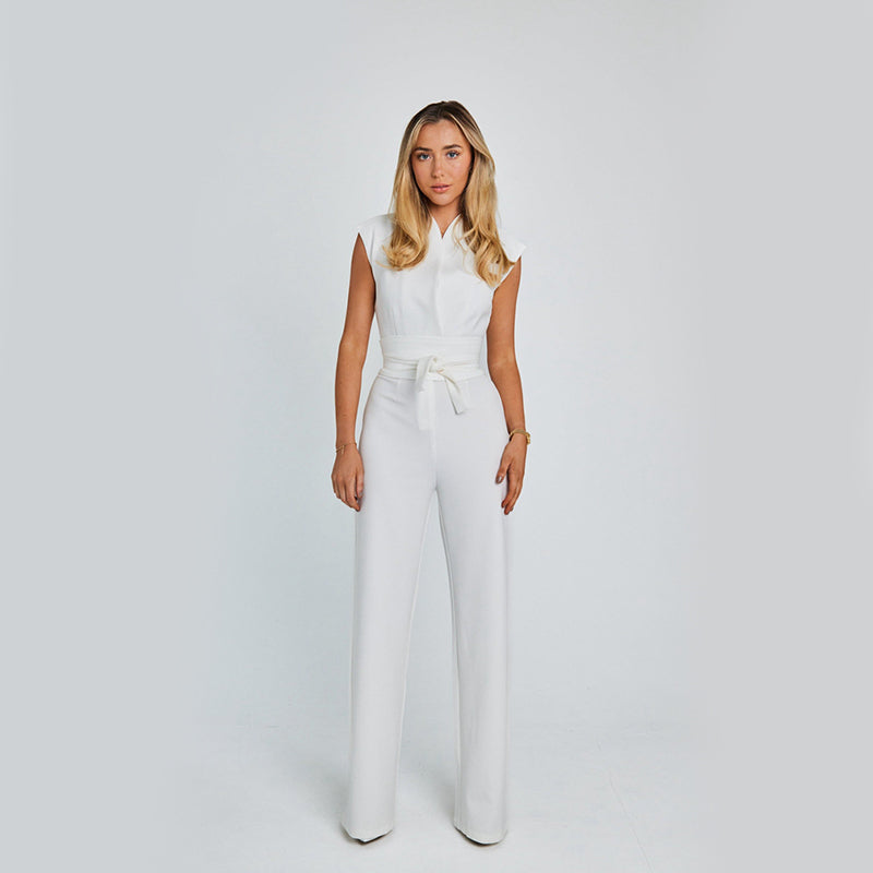Woman wearing a white sleeveless top and high-waisted pants on a plain background