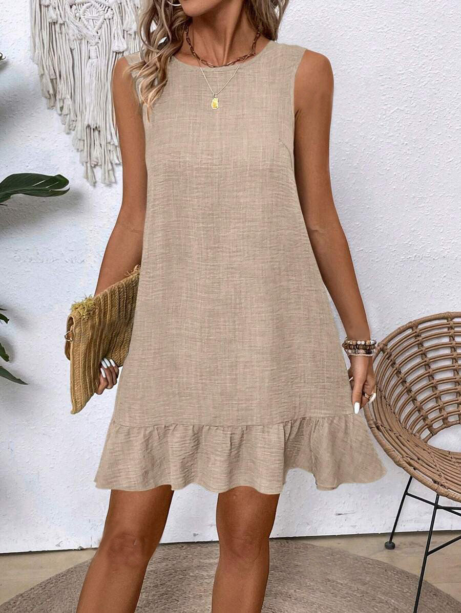 Woman wearing a beige dress with a white wall and decorative elements in the background
