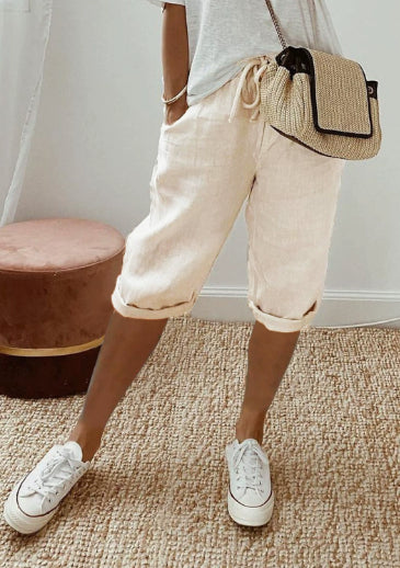 Person wearing beige shorts, white sneakers, and a straw bag indoors.