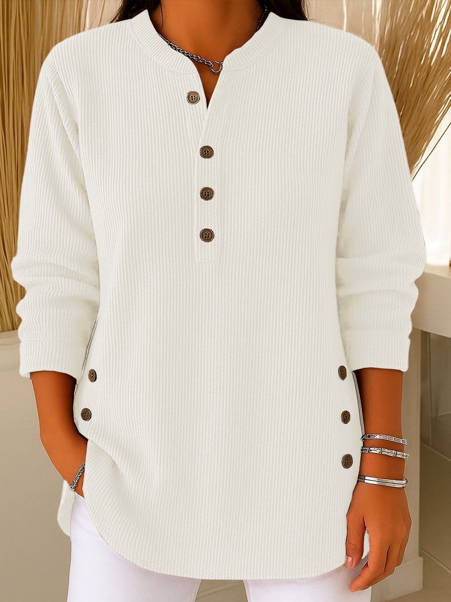 White ribbed sweater with brown buttons worn by a person, against a neutral background.