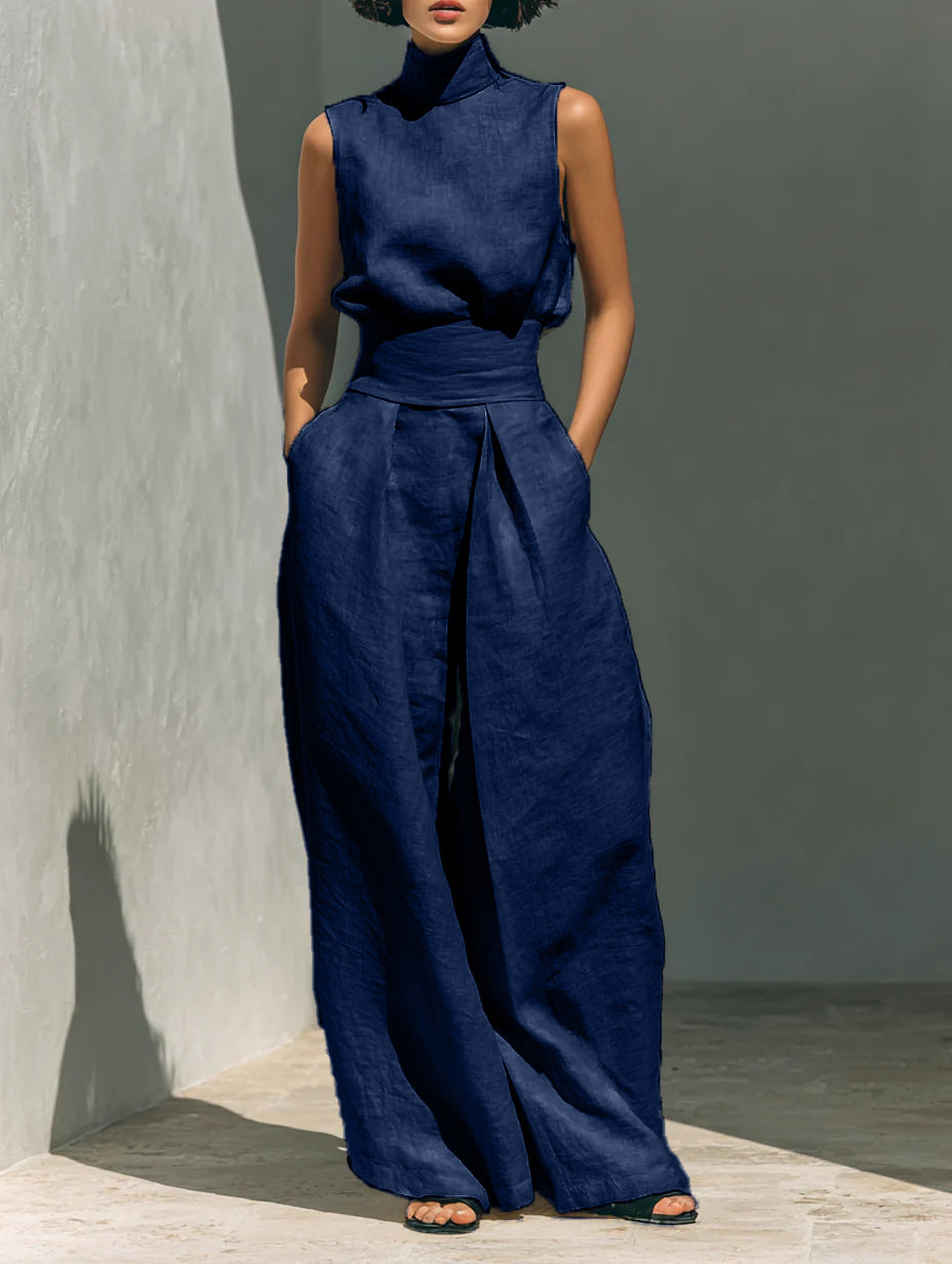 Person wearing a navy blue sleeveless top and wide-leg pants against a gray wall.