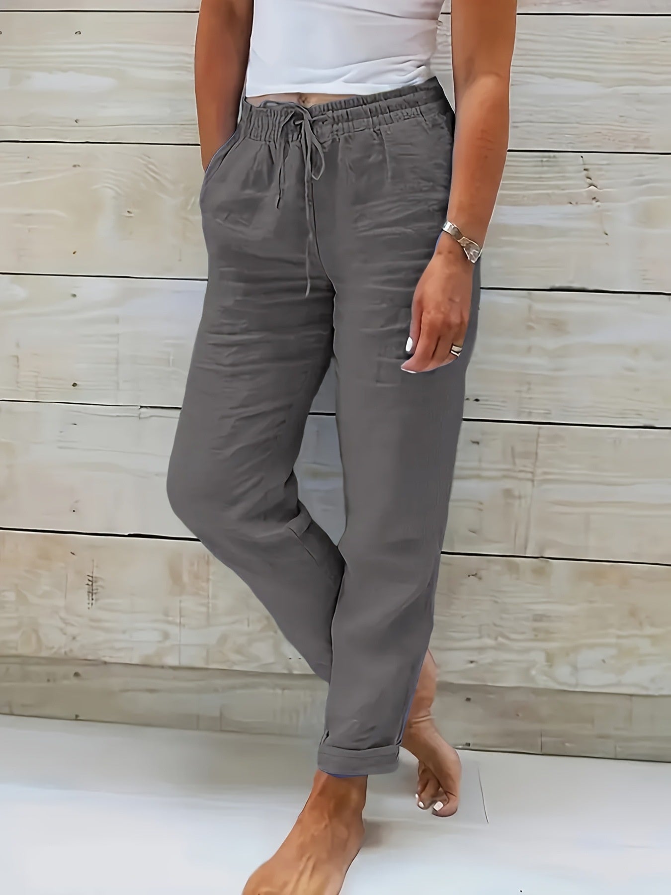 Person wearing gray pants with a white top against a wooden background