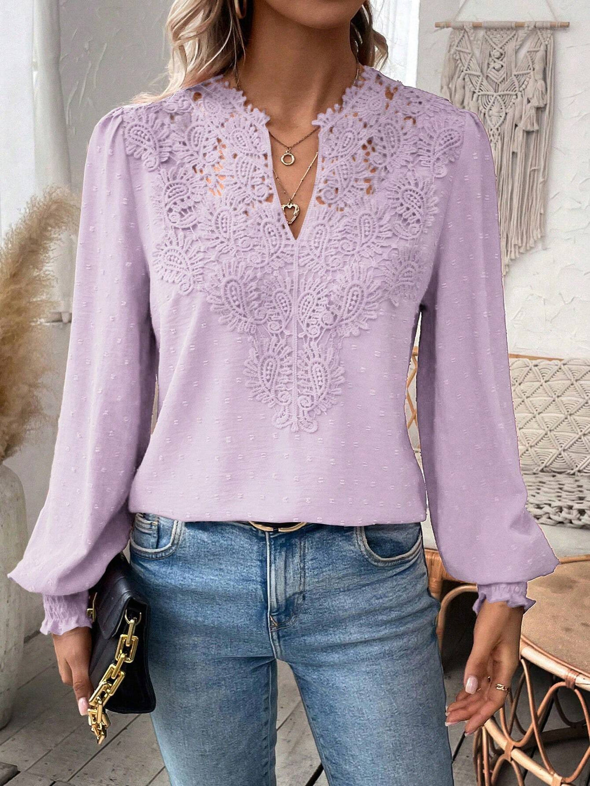 Person wearing a light purple blouse with lace details and blue jeans indoors.