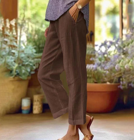 Person wearing brown pants standing in a garden with plants and flowers.