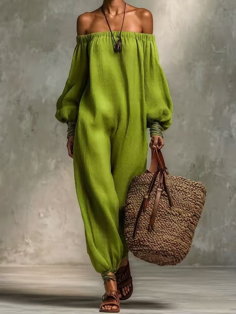 Person wearing a green off-shoulder top and high-waisted pants, holding a woven bag against a gray background.