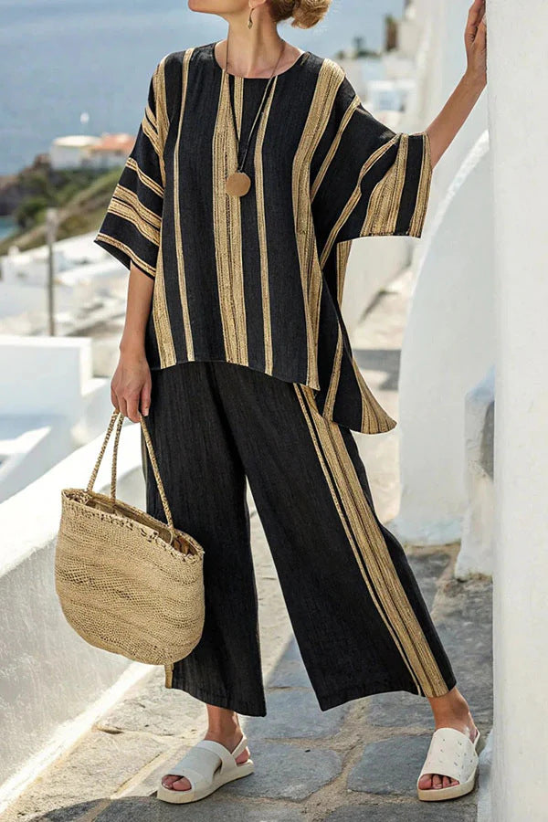 Woman wearing a black and beige outfit with wide-leg pants, standing on a sunlit street.