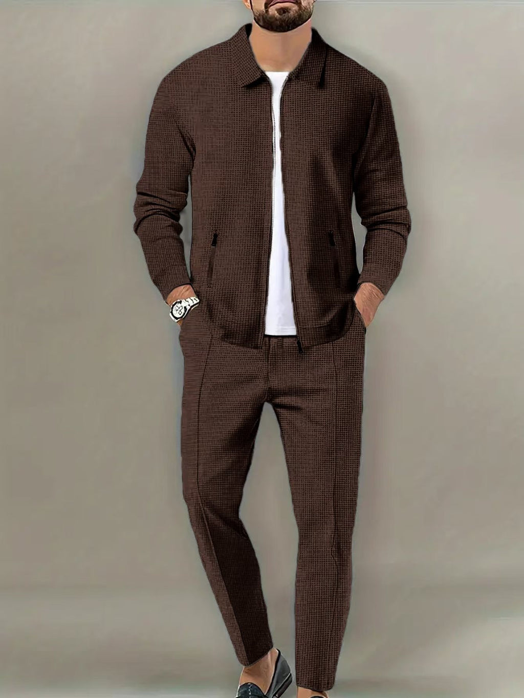 Man wearing a brown textured jacket and pants with a white shirt underneath on a plain background