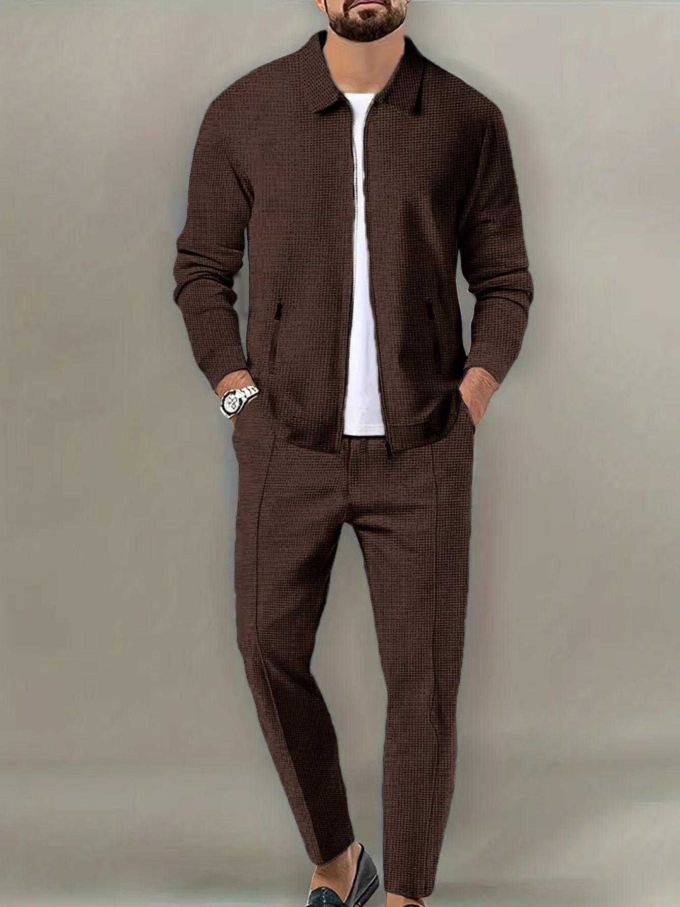 Man wearing a brown textured jacket and pants with a white shirt underneath on a plain background