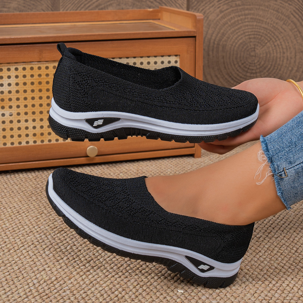 Black slip-on shoes with white soles worn by a person on a textured surface.