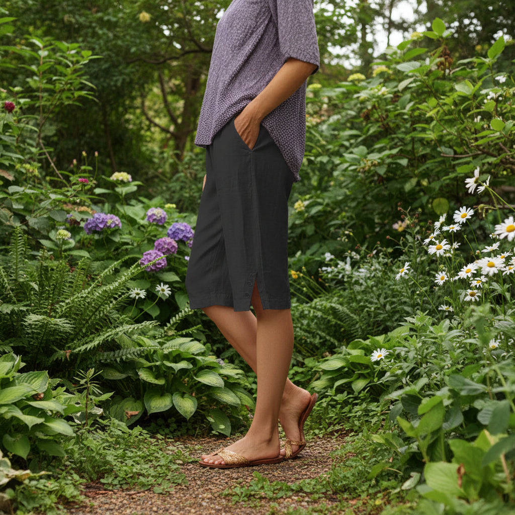Person wearing a patterned top and black capri pants standing in a garden setting.