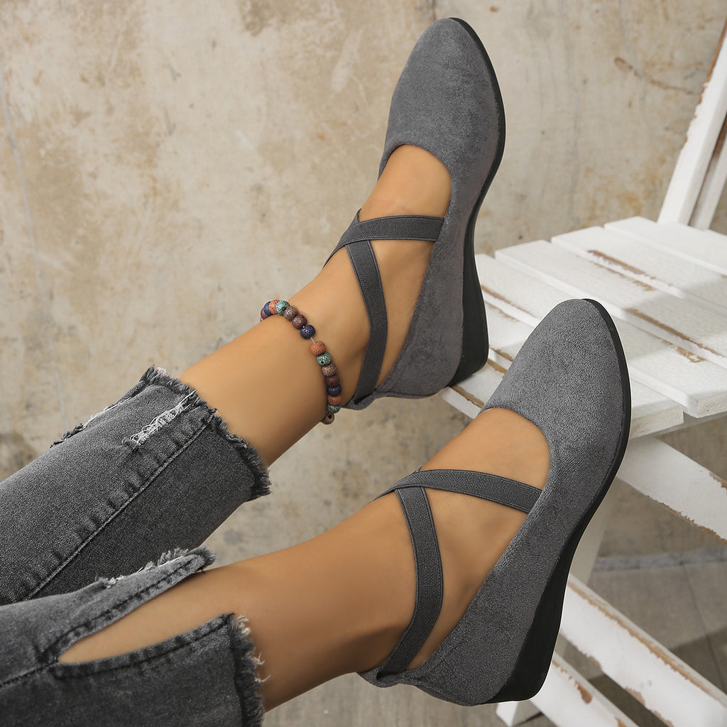 Gray suede shoes with thin straps worn by a person sitting on a white chair.