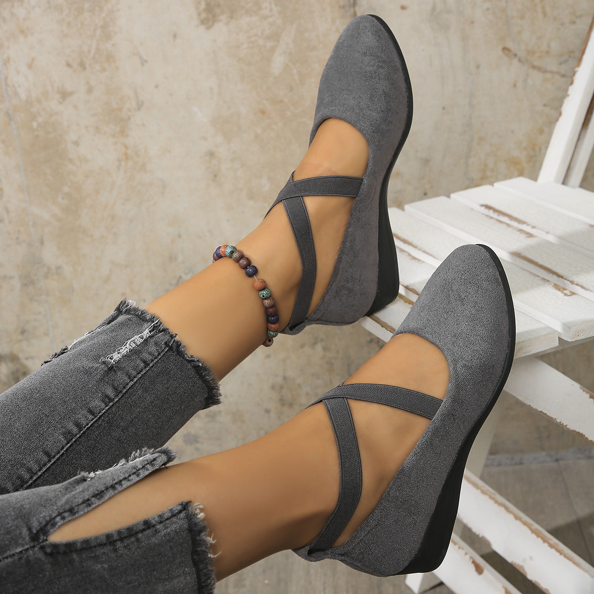 Gray suede shoes with thin straps worn by a person sitting on a white chair.