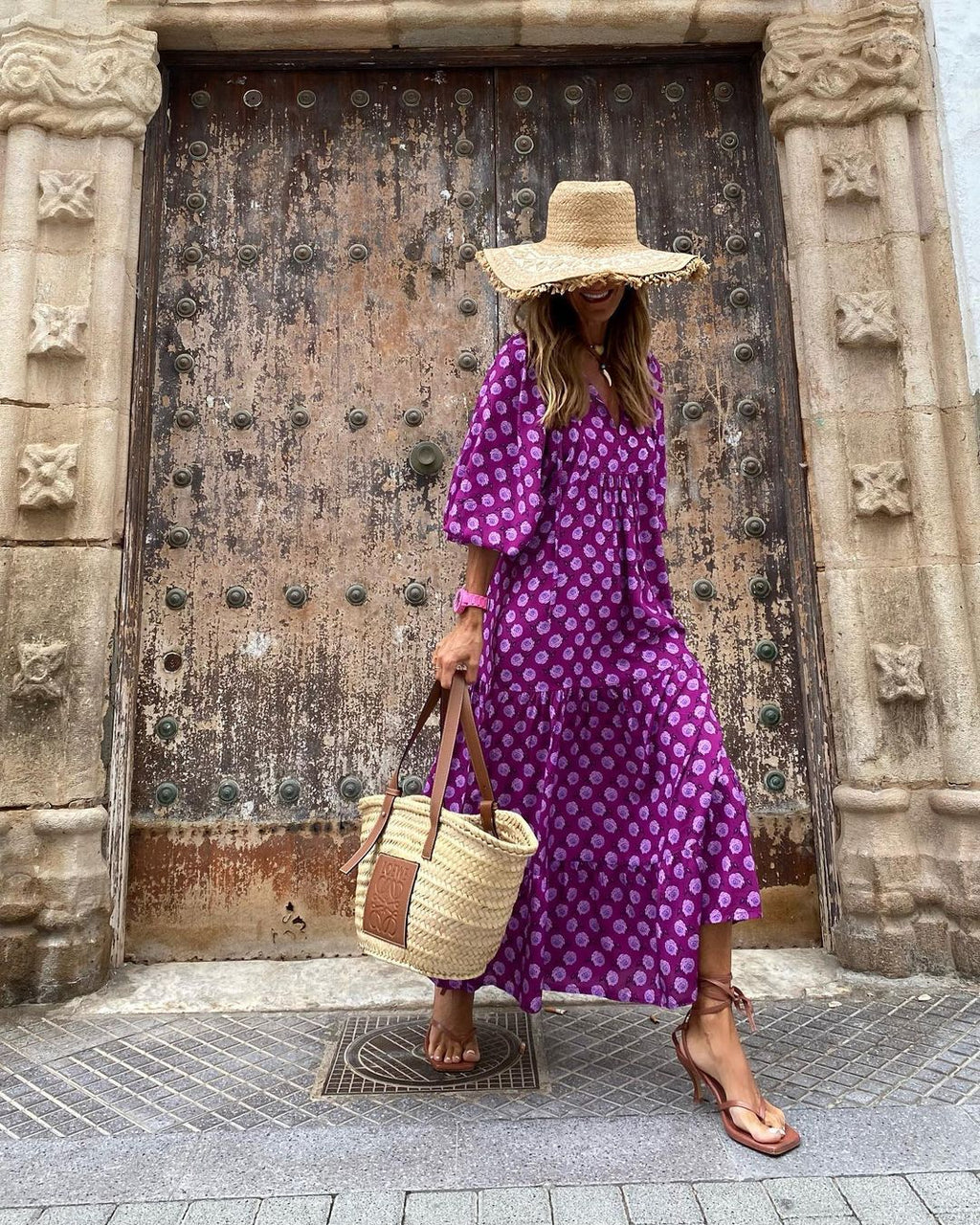 Woman in a purple dress with white polka dots standing in front of a large wooden door.