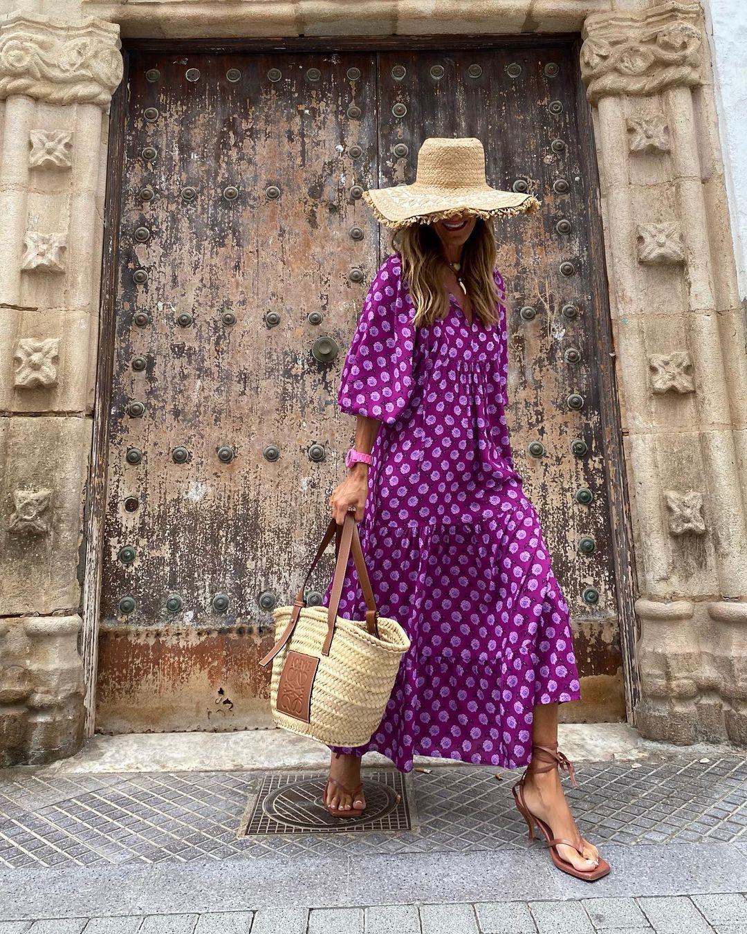 Woman in a purple dress with white polka dots standing in front of a large wooden door.