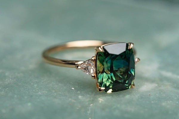 Gold ring with a green gemstone on a textured surface