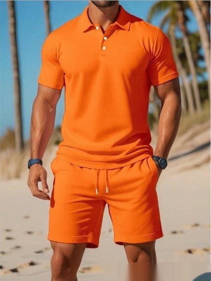 Person wearing an orange polo shirt and shorts set on a beach with palm trees in the background.