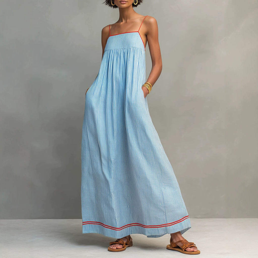 A woman models a light blue and white vertically striped maxi dress with thin spaghetti straps, a square neckline, and red piping accents along the neckline and hem. She is wearing brown leather slide sandals against a neutral gray studio background.