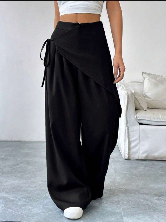 Person wearing black wide-leg pants with a white top in a minimalistic room.