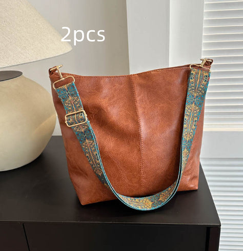 Brown leather handbag with a decorative strap on a dark surface.