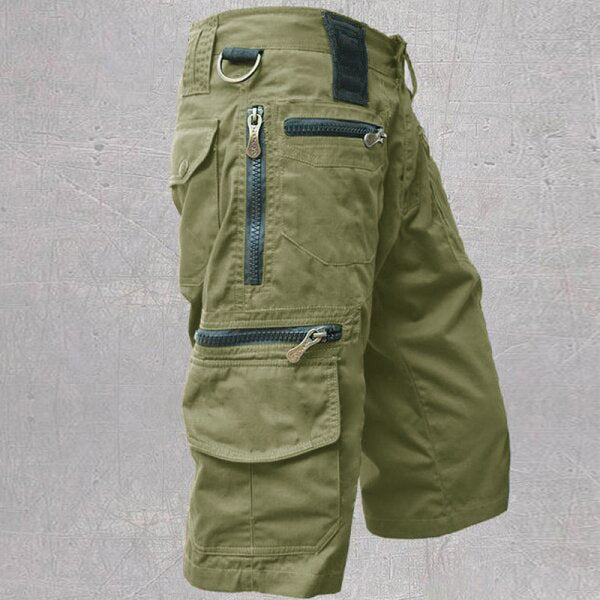 Green cargo shorts with multiple pockets and zippers on a gray background