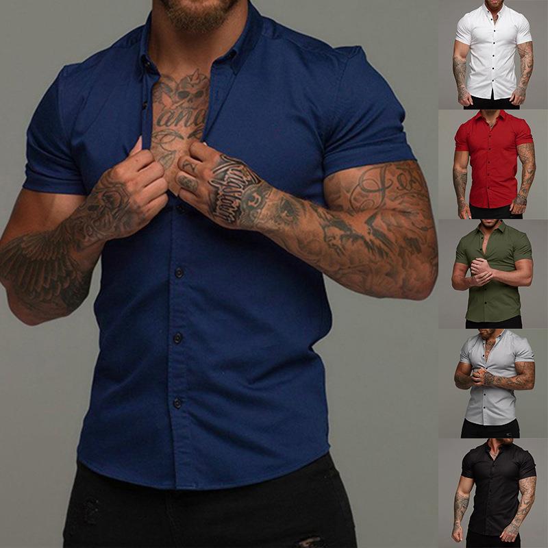 Man wearing a blue shirt with tattoos on arms, surrounded by other shirts in different colors.