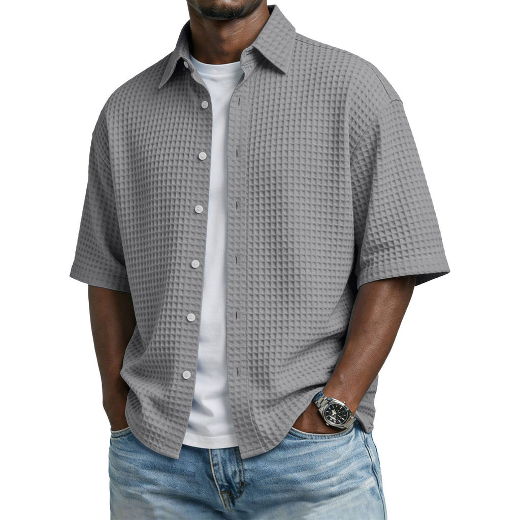Man wearing a gray textured short-sleeve shirt over a white shirt with blue jeans on a white background