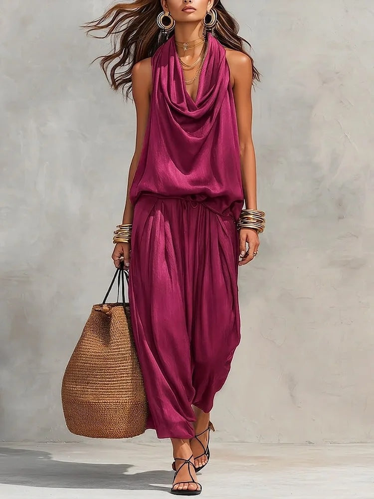 Woman wearing a magenta sleeveless top and pants with a woven bag against a gray background